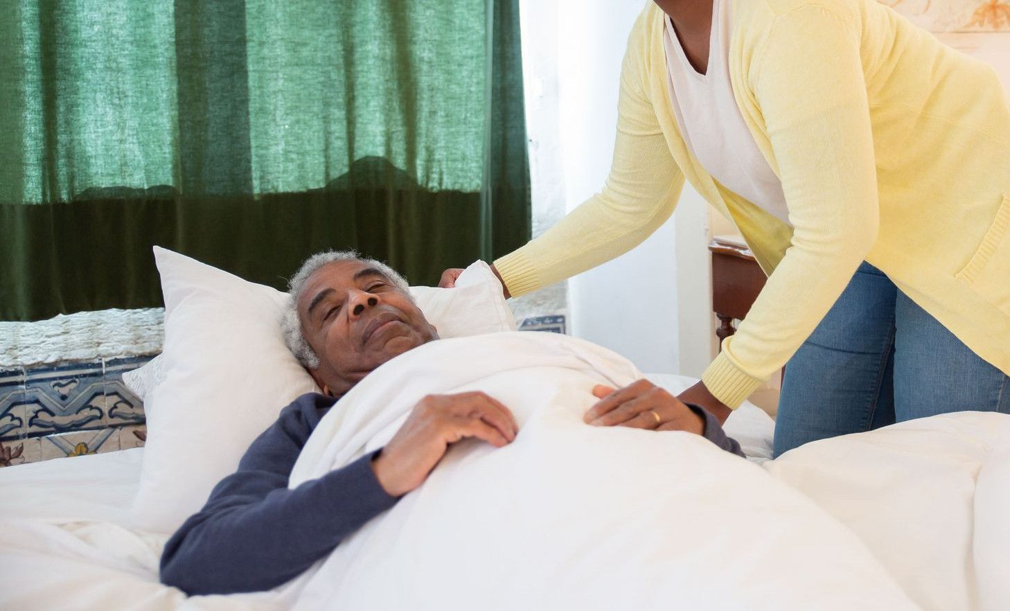 A woman tending to an elderly man in a bright and warm bedroom, symbolizing care and family support.
